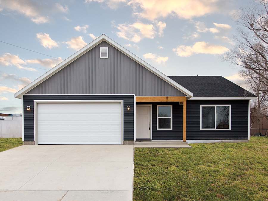 Marion model, depicting a single-story home with a modern exterior, a front porch, a two-car garage, and a well-maintained landscape with trees and shrubs.